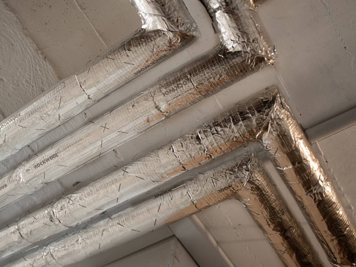 Gedämmte Heizungsleitungen mit Alukaschierung unter einer Kellerdecke, im rechten Winkel um eine Wandecke geführt
