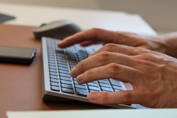 Hände tippen auf einer Tastatur am Schreibtisch.