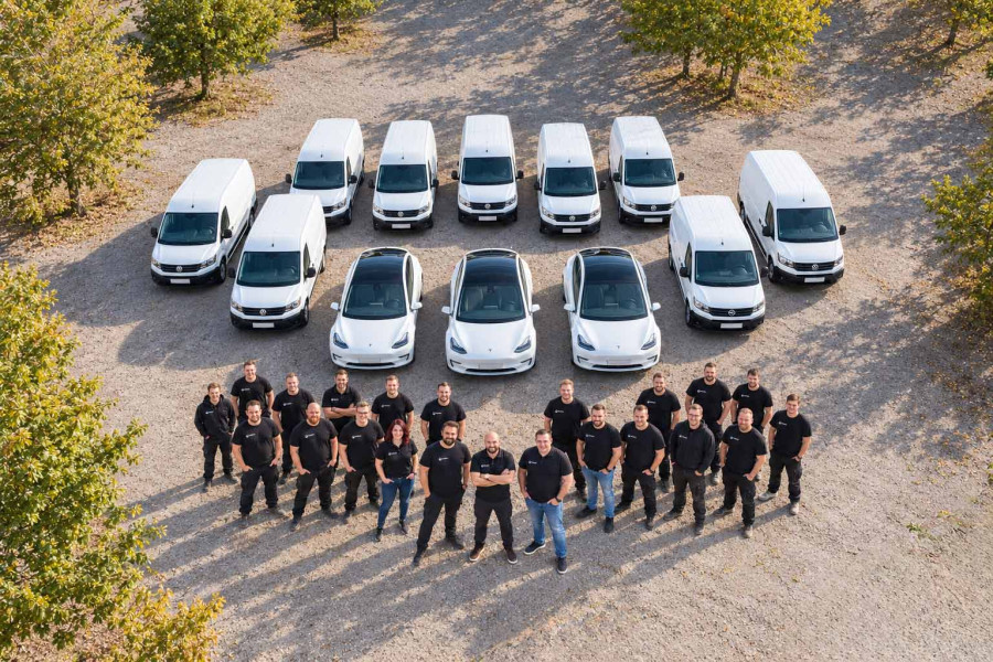 Luftaufnahme: das Team von TrioSan Hannover steht vor der Fahrzeugflotte aus weissen Transportern und drei Elektroautos