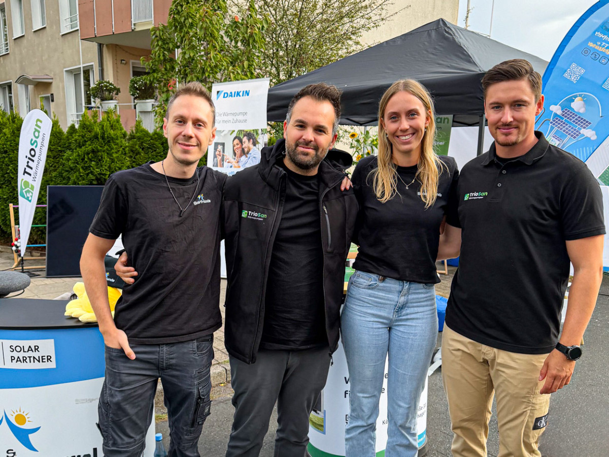 Zwei Mitarbeitende von TrioSan und zwei von Solarfreunde nebeneinander vor dem gemeinsamen Messestand bei einer Veranstaltung im Freien
